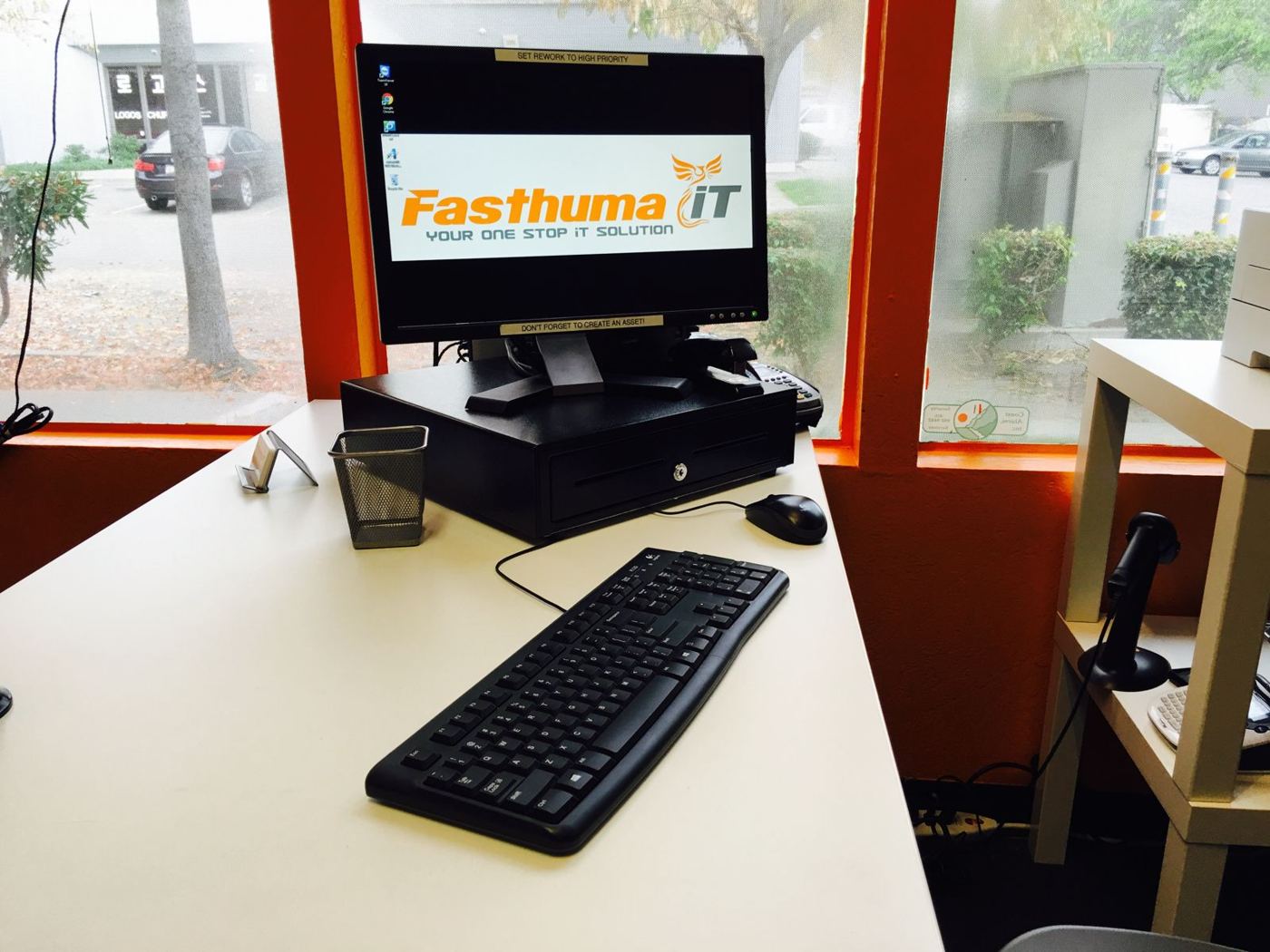 Front desk at the Fasthuma office with a computer screen showing the Fasthuma iT logo, a keyboard and a window to the parking lot
