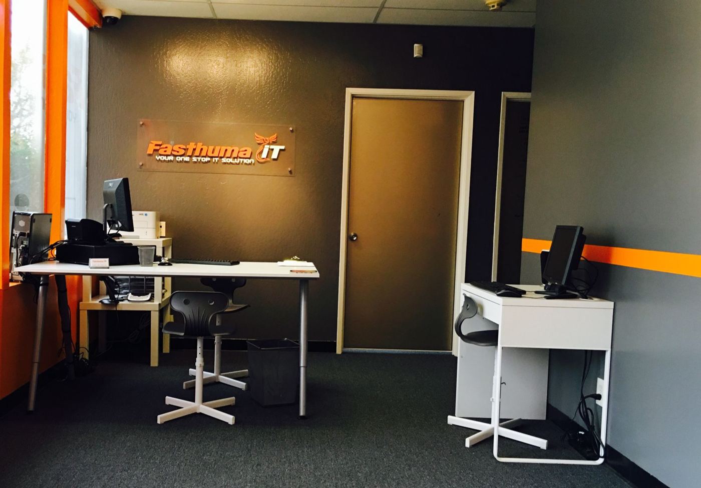 Inside the Fasthuma office in Fremont: two computer desks, a dark gray wall with the Fasthuma iT sign and an orange stripe