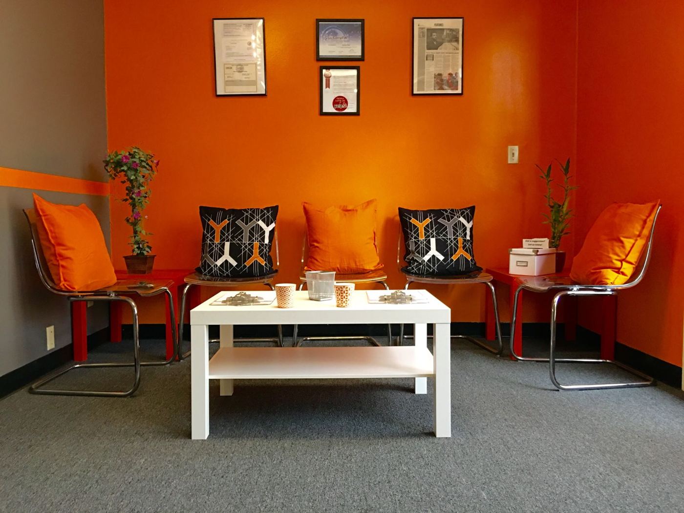 Fasthuma reception area with orange walls, chairs with orange and patterned cushions, a white coffee table and framed certificates